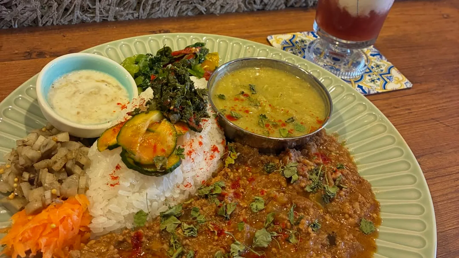 緑リムの皿に盛られたキーマカレーのワンプレートと、バルーン柄グラスのラッシー